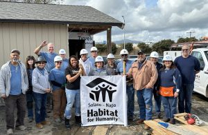 Board members volunteer at the build site and hold a logo sing of Solano-Napa Habitat for Humanity.